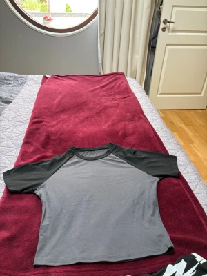 Två croppade t-shirts i svart och vitt - Säljer två croppade t-shirts, en i svart och grå med kontrastärmar och en i helvitt. Båda har rund hals och korta ärmar. Perfekta till jeans eller shorts för en avslappnad look.