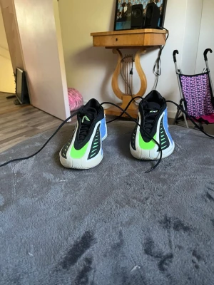 Färgglada sneakers med neon och blått - Säljer ett par unika sneakers basketskor  med vit sula, svart ovandel och detaljer i neonlime och blått. Skorna har snörning och coola grafiska linjer på sidorna. Perfekt för dig som vill sticka ut med din stil.