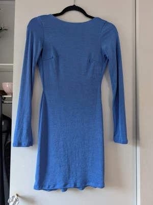 Blå långärmad kortklänning - En enkel och stilren blå klänning med lång ärm och kroppsnära passform. Klänningen är kort och tillverkad i ett mjukt, stretchigt material. Tyget är inte glittrig utan har ett skimmer i sig.