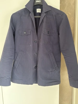 Mörkblå overshirt  - Stilren mörkblå overshirt från John Henric med raka linjer och klassisk krage. Två bröstfickor med knappstängning och två sidofickor. Tillverkad i ett mjukt bomullstyg som ger en avslappnad men snygg look. Perfekt att bära året om, den är vattentålig.