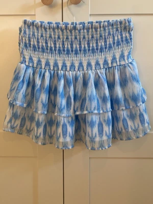Blåvit volangkjol från Gina Tricot  - Supersöt kort kjol i blått och vitt med smock i midjan och dubbla volanger i storleken 158/164. Kjolen har fint mönster och är gjord i ett lätt och luftigt material, perfekt för varma dagar. Passar till både sneakers och sandaler. Har bara använt en enstaka gång💕 45 kr + frakt
