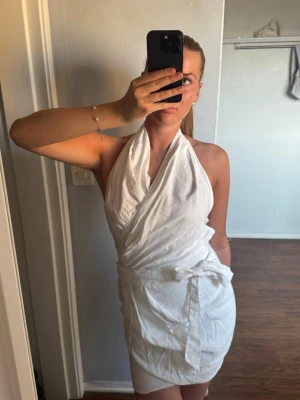 Vit linneklänning med knyt - Säljer en snygg vit halterneck linneklänning med  knyt i midjan och rygg. Klänningen är förliten för mig och kan därför inte visa bild bakifrån på. Superfin klänning och väldigt sommrig🌺