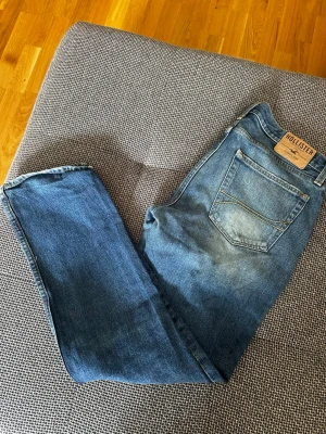 Blå bootcut jeans från Hollister - Snygga blå bootcut jeans från Hollister med klassisk femficksdesign och slitningar framtill. Jeansen har en läderpatch med logga bak i midjan och är tillverkade i denim med lätt stretch för skön passform.(pris kan diskuteras vid snabb affär)