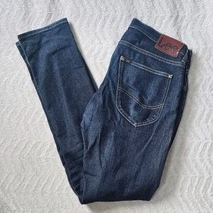Mörkblå jeans från Lee - Snygga mörkblå jeans från Lee med klassisk femficksdesign och kontrastsömmar. Jeansen har en rak passform och Lee-logga på bakfickan samt läderpatch i midjan. Perfekta för en avslappnad och trendig look.