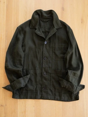 Mörkgrön Chore Jacket i linne - Stilren mörkgrön overshirt med tre stora fickor framtill och knäppning med fyra svarta knappar. Overshirten har klassisk krage och är tillverkad i ett luftigt linnematerial, perfekt för lager på lager. Passar dig som gillar en avslappnad men snygg look.