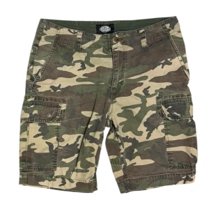 Dickies Camo Ripstop Cargo Shorts - Den här varan kommer auktioneras ut på Sneakershyllan x Plick Live den Torsdagen 16 juli kl 19. Dickies Camo Ripstop Cargo Shorts. Cargoshorts i camomönstrat ripstop-material från Dickies. Waist 32. Byxorna är välanvända med flera tecken på slitage och defekt som färgförlust, små hål etc.