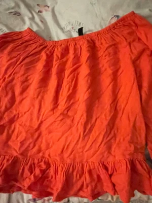 Orange offshoulder topp från Divided - Säljer en orange offshoulder topp från Divided med volangkant nedtill. Toppen har en lös passform och är perfekt för varma dagar. Tillverkad i ett lätt och luftigt material som känns skönt mot huden.