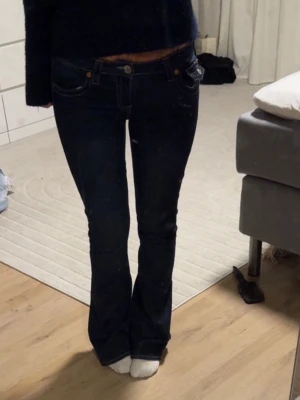 Bootcut jeans från True Religion - Mörkblå bootcut jeans från True Religion med klassiska kontrastsömmar och ficklock bak. Snygg passform som sitter tajt över låren och släpper ut vid vaden. Ikonisk logga på bakfickan och patch i midjan. Perfekta till sneakers eller boots.