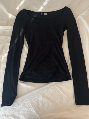 Svart långärmad topp från H&M - En svart långärmad topp från H&M med rund halsringning och figurnära passform. Toppen är enkel och stilren, perfekt att matcha med olika outfits. Tillverkad i mjukt material som känns skönt mot huden.