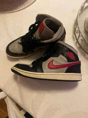 Jordans 39  - Snygga höga sneakers från Nike i svart och grått med en röd swoosh på sidan. Skorna har klassisk snörning, svart yttersula och detaljer i läder. Perfekta för dig som vill ha en streetwear-look med retrovibbar.