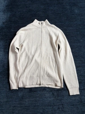 Beige ziptröja These Glory Days - Stilren beige ziptröja från These Glory Days i ribbstickad bomull. Perfekt för lager på lager och enkel att matcha med olika outfits. Använd 1 gång. Storlek S. Nypris 800kr