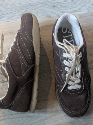 Bruna sneakers i mocka med vita detaljer - Bruna sneakers i mocka, retro design med mjuk innersula. Köpta på Asos och endast använda några gånger 🌹