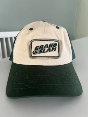 Grön och vit keps Grand Slam - Snygg keps i grönt och vitt med broderad Grand Slam-patch framtill och Björn Borg-logga baktill. Klassisk trucker-modell med mesh på baksidan och justerbar snapback. Perfekt för en sportig och avslappnad stil.
