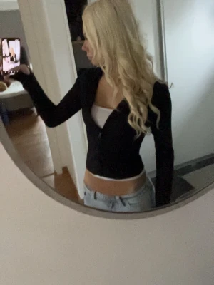 Svart tränings topp - Säljer en svart tränings top med långa ärmar. Toppen har en snygg knytning framtill och sitter tight. Perfekt att styla med jeans eller kjol för en trendig look. Kan förekomma sig lite nopprig