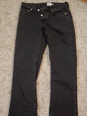 Svarta raka jeans - Säljer ett par svarta jeans med rak passform och klassisk femficksdesign. Jeansen har silverfärgade knappar och nitar samt bälteshällor i midjan. Perfekta för en clean och stilren look.