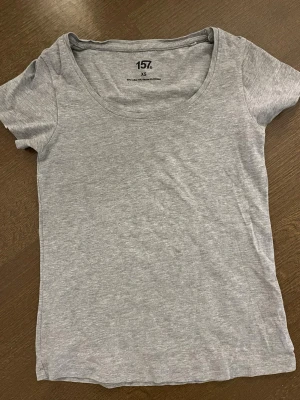 Ljusgrå basic t-shirt från 157 - En enkel och stilren ljusgrå t-shirt från 157 med rund halsringning och korta ärmar. Tillverkad i mjuk bomull som känns skön mot huden. Perfekt att matcha med jeans eller kjol för en clean look.