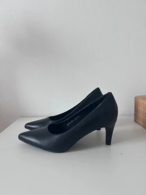 Svarta klassiska pumps med spetsig tå - Stilrena svarta pumps med spetsig tå och smal klack. Skorna har en elegant siluett och är tillverkade i ett slätt material som ger en tidlös look. Perfekta för dig som gillar enkel och klassisk stil.