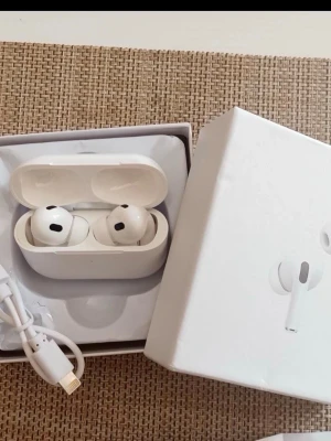 Airpods gen 2 - Säljer ett par vita trådlösa in-ear hörlurar med laddningsetui. Hörlurarna har en stilren och kompakt design med silikonproppar för bra passform. Perfekta för musik, poddar och samtal på språng.