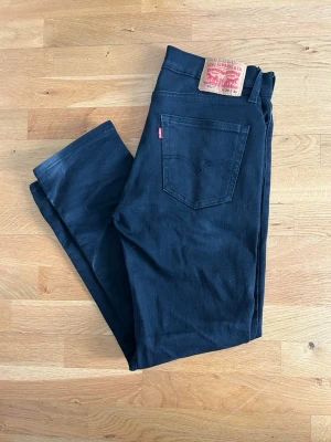 Svarta Levi's 511 jeans - Säljer ett par svarta Levi's 511 jeans med smal passform och klassisk femficksdesign. Jeansen har en snygg svart tvätt och är tillverkade i ett mjukt och stretchigt bomullsmaterial. Perfekta för en stilren och avslappnad look.