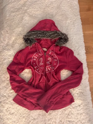 Rosa hoodie med päls från Hollister - Mysig rosa hoodie från Hollister med ett tryckt märke på, i storlek xs