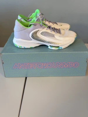 Nike Giannis Immortality sneakers - Snygga Nike Giannis Immortality sneakers i vitt och ljusgrått med detaljer i silver och limegrönt. Skorna har mesh- och syntetmaterial för bra andningsförmåga och komfort. Låg modell med cool design och gröna innersulor. Bra för basket använda cirka 4 gånger,box medföljer 