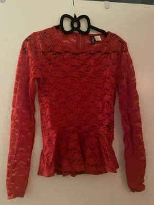 Röd spetsblus med volang - Säljer en röd långärmad blus i spets med volang nertill. Blusen har rund halsringning och dragkedja i ryggen. Tunn och genomskinlig spets ger en snygg look, perfekt att styla med jeans eller kjol. Det är storlekek 38 men skulle säga att den är söm 34/36 