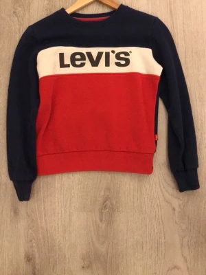 Levi's färgglad sweatshirt utan huva - Säljer en snygg sweatshirt från Levi's i färgerna marinblå, röd och vit. Tröjan har en klassisk rund halsringning och stor Levi's-logga framtill. Perfekt för dig som gillar streetwear och vill sticka ut med en färgstark look.