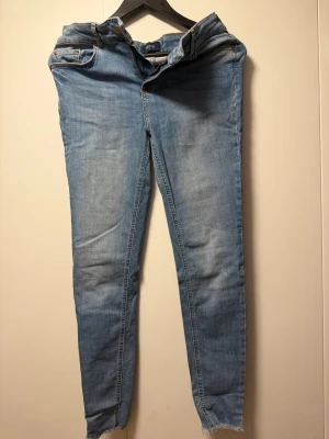 Ljusblå skinny jeans från Pieces - Säljer ett par ljusblå skinny jeans från Pieces med klassisk femficksdesign och råa kanter vid bensluten. Jeansen har hög midja och är tillverkade i stretchigt denimtyg för en bekväm passform.