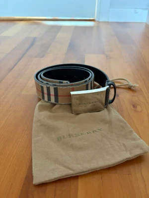 Burberry bälte med klassiskt rutmönster - Snyggt Burberry bälte med det ikoniska beige, svarta och röda rutmönstret. Bältet har en silverfärgad metallspänne med Burberry-logga och svart insida. Bältet är väl använt som du kan se på bilden men inget man tänker på när det sitter på. Köpt på NK för 3000 ungefär men för flera år sedan. Säljs till riktigt bra pris!!