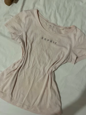 Ljusrosa Esprit t-shirt med strass - Snygg ljusrosa t-shirt från Esprit med rund halsringning och dekorerad med strassbokstäver på bröstet. T-shirten är figursydd och gjord i mjukt bomullsmaterial. Perfekt för en avslappnad och trendig look.