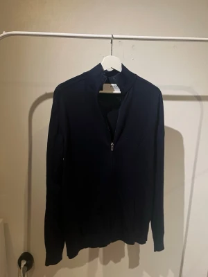 Marinblå ziptröja - Stilren marinblå ziptröja från Selected Homme med dragkedja framtill. Tröjan har en enkel design och är tillverkad i ett mjukt material som passar perfekt till lager på lager. Perfekt för dig som gillar minimalistisk stil.