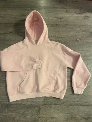 Ljusrosa hoodie från 157, storlek M - Ljusrosa hoodie från 157 med klassisk känguruficka och huva. Tillverkad i mjukt sweatshirtmaterial som är perfekt för chill dagar. Ribbade muddar vid ärmslut och nederkant ger en skön passform. Enkel och stilren design som passar till det mesta.
