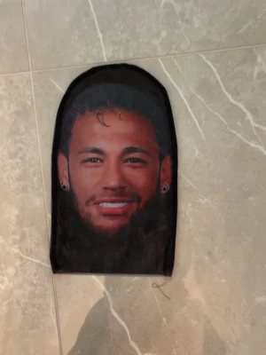 Svart balaclava med Neymar - Säljer en svart balaclava i stretchigt tyg med tryckt motiv framtill. Passar perfekt för dig som vill ha en unik och edgy accessoar till din outfit. Materialet är mjukt och följsamt.