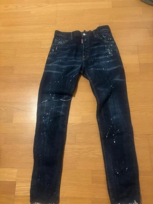 Mörkblå Dsquared2 jeans med slitningar - Säljer ett par mörkblå jeans från Dsquared2 med slitningar och färgstänk,hör av er vid intresse!