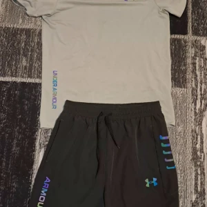 Svarta träningsshorts från Under Armour - Snygga svarta träningsshorts från Under Armour med färgglad logga och text längs benet. Shortsen har elastisk midja med snörning för bästa passform och är tillverkade i ett lätt och snabbtorkande material som passar perfekt till träning.