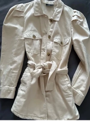 Beige jeans jacka med puffärm och knytskärp - Trendig beige overshirt med puffärmar, knappar framtill och två bröstfickor. Jackan har ett knytbart bälte i midjan💕💕. Använd 1 gång 💞ordinarepris 499kr
