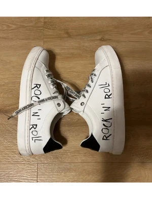  Zadig & Voltaire skor - Snygga vita sneakers från Zadig & Voltaire med signatur loggan rock n roll skrivet på sidan. Super snygga till våren och sommaren.