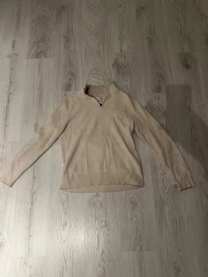 Beige stickad tröja med halvzip - Säljer en beige stickad tröja från These Glory Days i storlek S. Tröjan har en halvzip-dragkedja vid halsen och är ribbstickad i mjukt material. Perfekt för lager på lager och enkel att matcha med olika outfits.