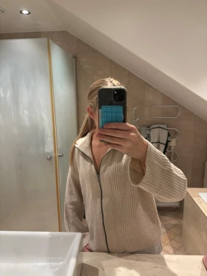 Beige stickad ziptröja med krage - Mysig beige stickad ziptröja med hög krage och långa ärmar. Tröjan har en grovstickad struktur och dragkedja framtill. Perfekt för lager på lager och chill dagar. Materialet ser ut att vara mjukt och värmande, troligen bomull eller ullmix.