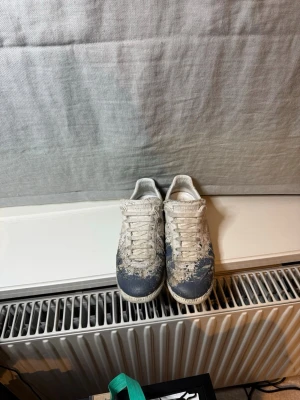 Vita och blå sneakers med snörning - Säljer ett par vita sneakers med blå detaljer och klassisk snörning. Skorna har en låg profil och en enkel, stilren design som passar till många olika outfits. Materialet är textil och syntet. Perfekta för dig som gillar en avslappnad streetstil.