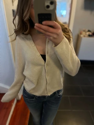 Beige kofta med v-ringning - Mysig beige kofta med v-ringning och knappar framtill. Koftan har en avslappnad passform och långa ärmar, perfekt att slänga på sig över ett linne eller t-shirt. Passar till jeans för en chill look.