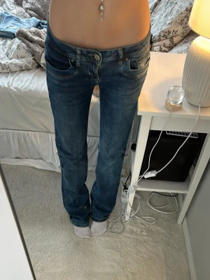 Blå bootcut jeans med låg midja - Säljer ett par klassiska blå bootcut jeans med låg midja och kontrastsömmar för en cool look. Perfekta till vardagsstilen och passar till det mesta. 37cm raktöver midjan 
