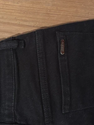 Svarta bootcut jeans från Ateen  - Säljer ett par svarta bootcut jeans från Ateen. Jeansen har klassisk femficksdesign, bälteshällor och en metallogo bak. Materialet är mjukt och stretchigt, perfekt för en snygg och bekväm look.