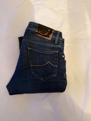 Mörkblå jeans från Jacob Cohen - Snygga mörkblå jeans från Jacob Cohen med klassisk femficksdesign och kontrastsömmar. Jeansen har en patch med logga bak och knappgylf framtill. Tillverkade i mjukt denimtyg som sitter skönt och har en modern passform. W29 Mått, midja-39,5, längd-98. 