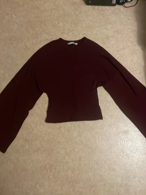 Mörkröd croppad tröja med vida ärmar - Säljer en mörkröd croppad tröja med breda, vida ärmar och rund halsringning. Tröjan har en enkel och stilren design som passar perfekt till jeans eller kjol. Materialet känns mjukt och stretchigt, vilket gör den bekväm att bära.
