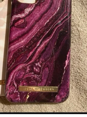 Ideal of Sweden Mobilskal - Snyggt mobilskal från iDeal of Sweden med ett mörklila och rosa marmormönster. Skalet har en glansig finish och en guldfärgad logga längst ner. Tillverkat i hårdplast som skyddar mobilen och ger en lyxig känsla. Säljs tillsammans med andra mobil skal också!!🩷🩷