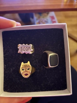 Maria Nilsdotter , Tre unika ringar - Säljer  tre coola ringar: en silverfärgad ring med svart rektangulär sten, en guldfärgad ring med batgirl och glittriga ögon och röd mun samt en silverfärgad ring med texten 'BOOM' i serietidningsstil. Perfekta för dig som vill sticka ut och addera lite edge till din stil samt limiterade släpp från Nilsdotter. 750-1500kr styck. 