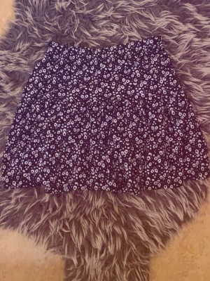 Svart blommig kjol - Söt svart kjol med vitt blommönster. Kjolen har en lätt utställd form och resår i midjan för skön passform. Perfekt för dig som gillar en avslappnad men ändå trendig stil.