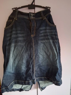 Mörkblå jeanskjol med fickor - Snygg mörkblå jeanskjol i klassisk modell med fram- och bakfickor samt kontrastsömmar. Kjolen har knapp- och dragkedjestängning framtill och är tillverkad i slitstarkt denimtyg. Perfekt för en avslappnad och trendig look.