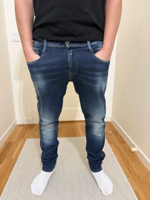 Blå slim jeans från Replay  - Säljer ett par blå slim jeans från Replay med avslappnad passform och låg gren. Jeansen har slitningar och ljusa tvättade partier framtill och baktill, samt klassiska fem fickor och läderpatch bak i midjan. Perfekta för en chill och trendig stil.